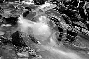 Black and White Slow Shutter Speed Photography of a Small River with Moss Covered Rocks in the Woods.