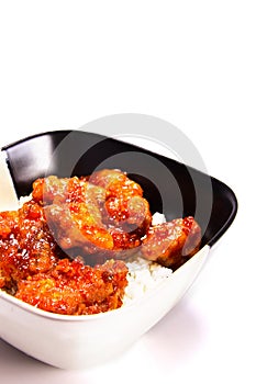 A black and white squre ceramic bowl filled with white rice and orange chicken.