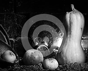 A black and white still life image with a pumpkin, apples and an alarm clock.