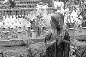 Black and white stone statue of Buddhist monk standing and praying