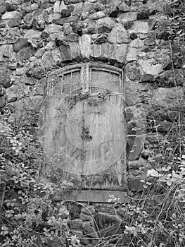 Black and white stone wall surrounds abandoned shuttered window with vines