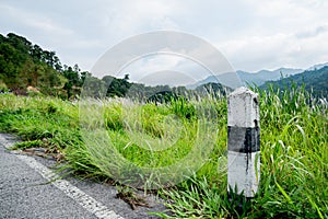 Black and white stones  concrete pillar kilometers on the road are covered with grass. With a gray sky, rocky kilometers on the