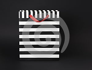 Black and white stripped gift-bag with red satin handles, on a black background.