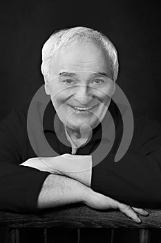 Black and white studio portrait of a brown-eyed smiling elderly handsome man with white gray hair in black clothes; up to the