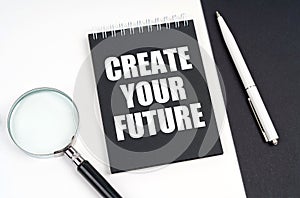 On a black and white surface lies a magnifying glass, a pen and a notepad with the inscription - Create Your Future