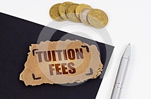 On a black and white surface lies a pen, coins and a cardboard sign with the inscription - Tuition Fees