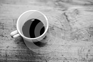 Black and white textured photo; close-up of ceramic cup with coffee on wooden table.