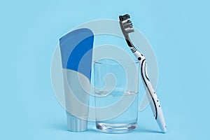 A black and white toothbrush with toothpaste and glass of mouthwash on blue background with copy space