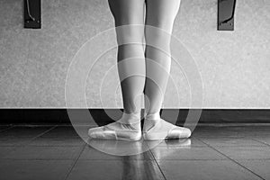 Black and white version of back view of ballet dancer ballerina at the barre in dance class standing in first position