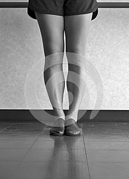Black and white version of dancer`s legs in jazz first position at the barre