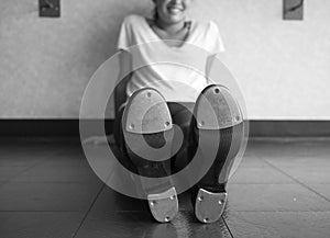 Black and white version of Smiling tap dancer sitting on the dance studio floor in her tap shoes