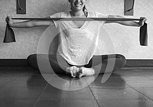 Black and white version ofSmiling Young Active Female using a theraband exercise band to strengthen her arms muscles in the studio photo