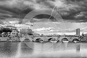 Black and white view of the ancient Bridge of Augustus and Tiberius in the historic center of Rimini, Italy, under a stormy sky