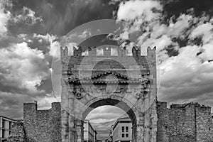 Black and white view of the Arch of Augustus in Rimini, Italy, the oldest extant Roman arch, against a dramatic sky