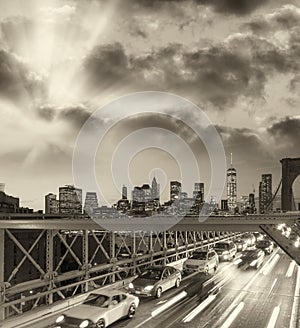 Black and white view of cars speeding up at night over Brooklyn Bridge, New York City