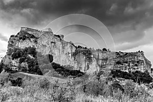 Black and white view of the imposing fortress of San Leo, Emilia Romagna, Italy, under a stormy sky with rain clouds