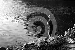 Black and white view of male fisherman angling in river. Angler fishing by river.