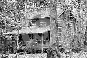 A black and white view of an old log cabin in the mountains.