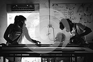 Black and white view of a young couple of carpenter working together in a wood workshop. Couple handcrafting new furniture made of