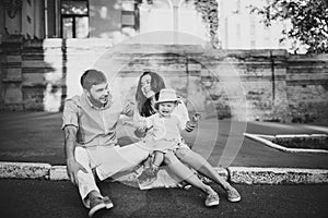 Black and white. Young stylish couple sit on the pavement in old town. Handsome boy happy with his parents