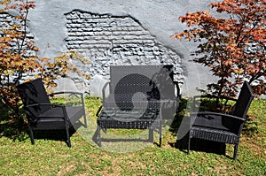 Black wicker patio furniture in the garden in front of a grey brick wall