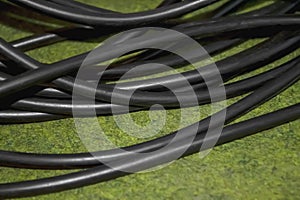 Black wire on the green carpet. A thick wire of black color in a winding on a green carpet. There is a reeled black