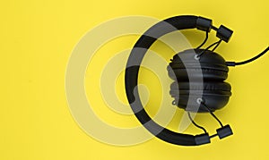 Black wired headphones on a yellow background. Overhead, isolated professional-grade headphones for DJs and musicians