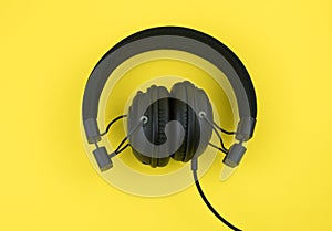 Black wired headphones on a yellow background. Overhead, isolated professional-grade headphones for DJs and musicians