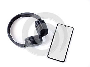 Black wireless headphone and mobile smartphone with a blank screen mockup lay on the surface of a white background