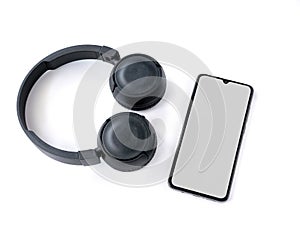 Black wireless headphone and mobile smartphone with a blank screen mockup lay on the surface of a white background