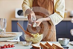 Black woman adding spices to pasta cooking in kitchen