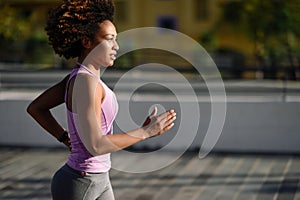 Black woman, afro hairstyle, running outdoors in urban road.