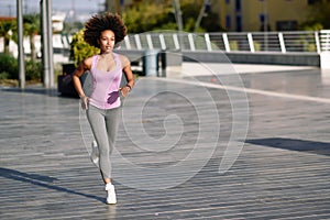 Black woman, afro hairstyle, running outdoors in urban road.