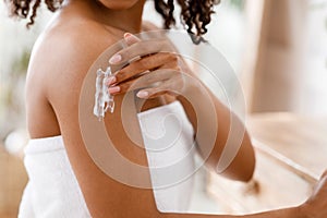 Black woman applying moisturizing body lotion on skin after shower