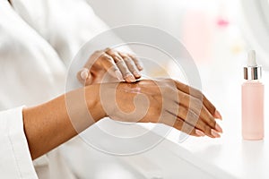 Black woman applying serum to her hands at home