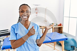 Black woman with braids working at pain recovery clinic showing palm hand and doing ok gesture with thumbs up, smiling happy and