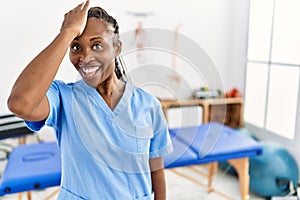 Black woman with braids working at pain recovery clinic surprised with hand on head for mistake, remember error