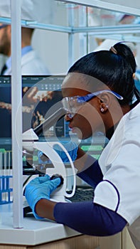 Black woman chemist analysing reaction of virus on microscope