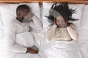 Black woman closing ears tired of her husband`s noisy snoring.