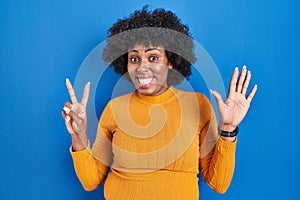 Black woman with curly hair standing over blue background showing and pointing up with fingers number seven while smiling