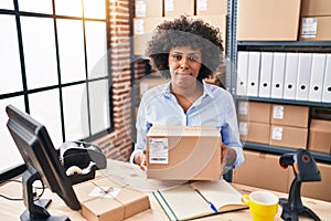 Black woman with curly hair working at small business ecommerce holding box relaxed with serious expression on face