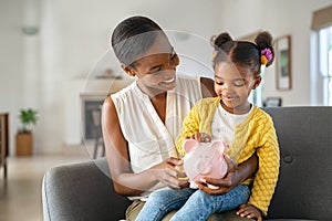 Black woman with daughter holding piggy bank