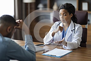 Black woman doctor having conversation with upset sick man patient