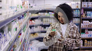 Black woman doing grocery shopping in supermarket, looking at full shelves buying food