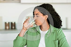 Black woman enjoys refreshing glass of water in kitchen indoors