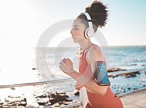 Black woman, fitness and running with headphones and cellphone on arm at the beach in Cape Town. Sporty African American