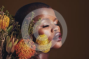 Black woman, flowers and makeup in studio for beauty, wellness or thinking with protea by brown background. Girl, model