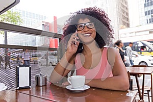 Black woman with frizzy hair using cell phone outdoors and having a cup of coffee in Sao Paulo during summer, urban background.