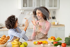 Black woman giving high five to girl in kitchen