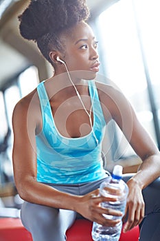 Black woman, gym or earphones with water for fitness, break or body recovery after training. Listen, thinking or athlete